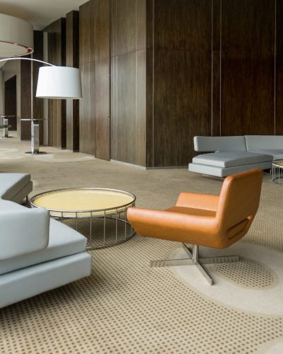 Modern hotel lobby with hallway or office lounge room. Interior with wood paneling, leather sofa and chairs, round metallic tables and floor lamp. Downtown workspace design concept